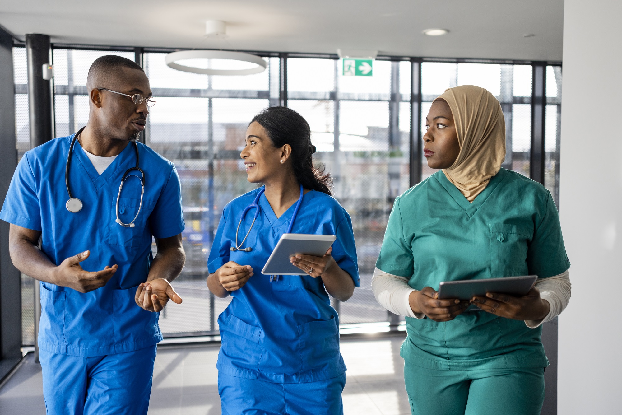 Three nurses in scrubs walk and talk in a hospital